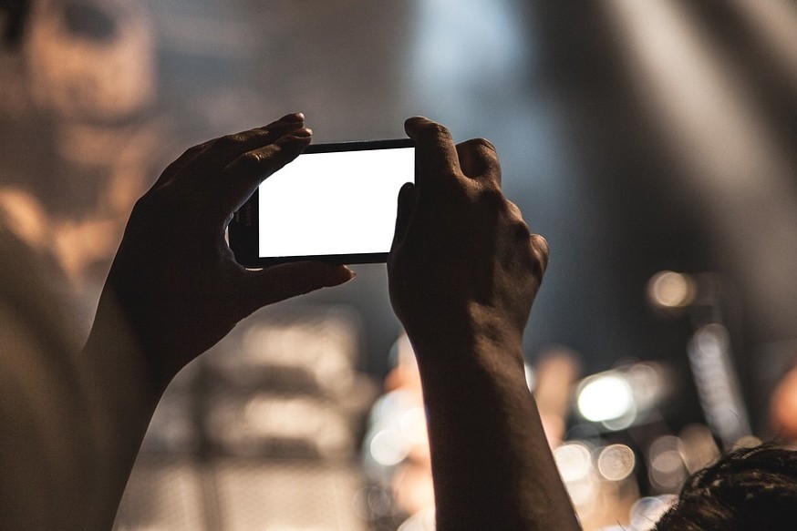 Mani che tengono uno smartphone e filmano un palco