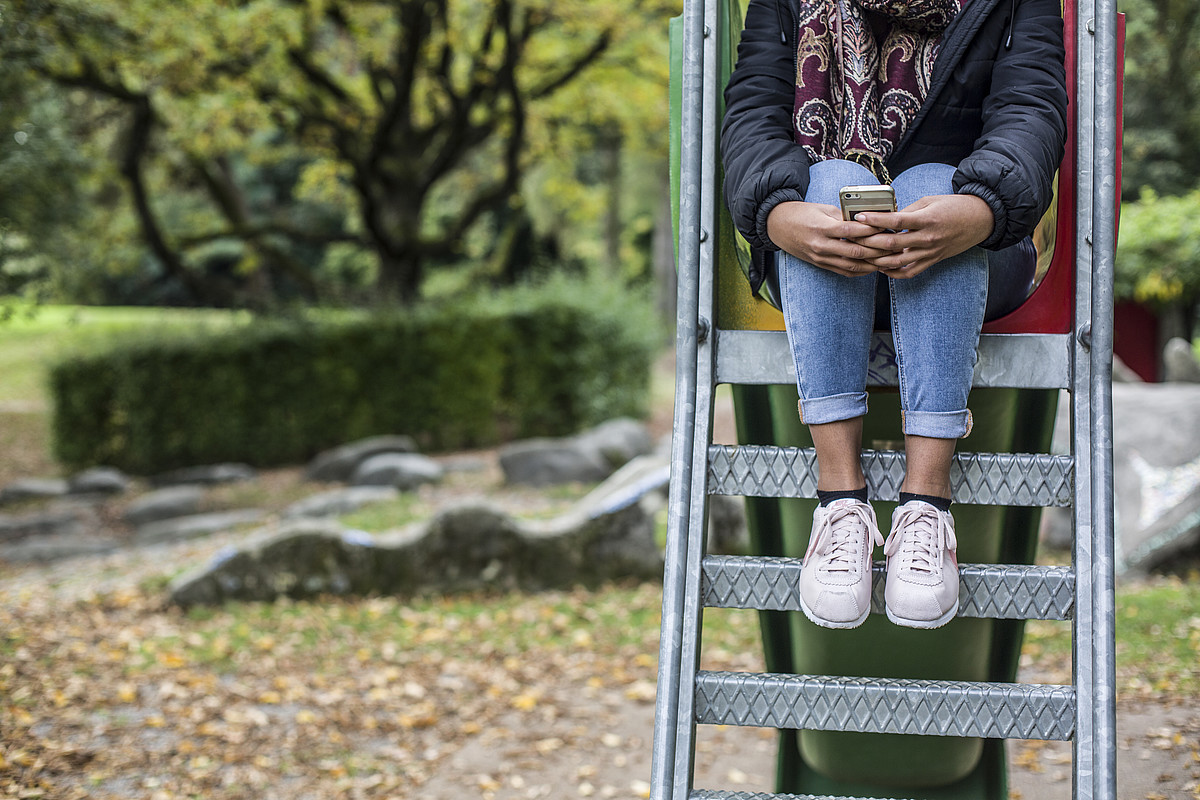 Una ragazza è seduta sui gradini di uno scivolo, stringendo forte il cellulare.