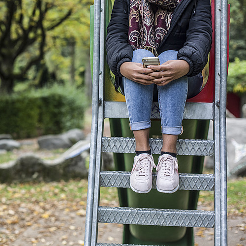 Un'adolescente è seduta sulla scaletta di uno scivolo. Stringe forte il suo cellulare.